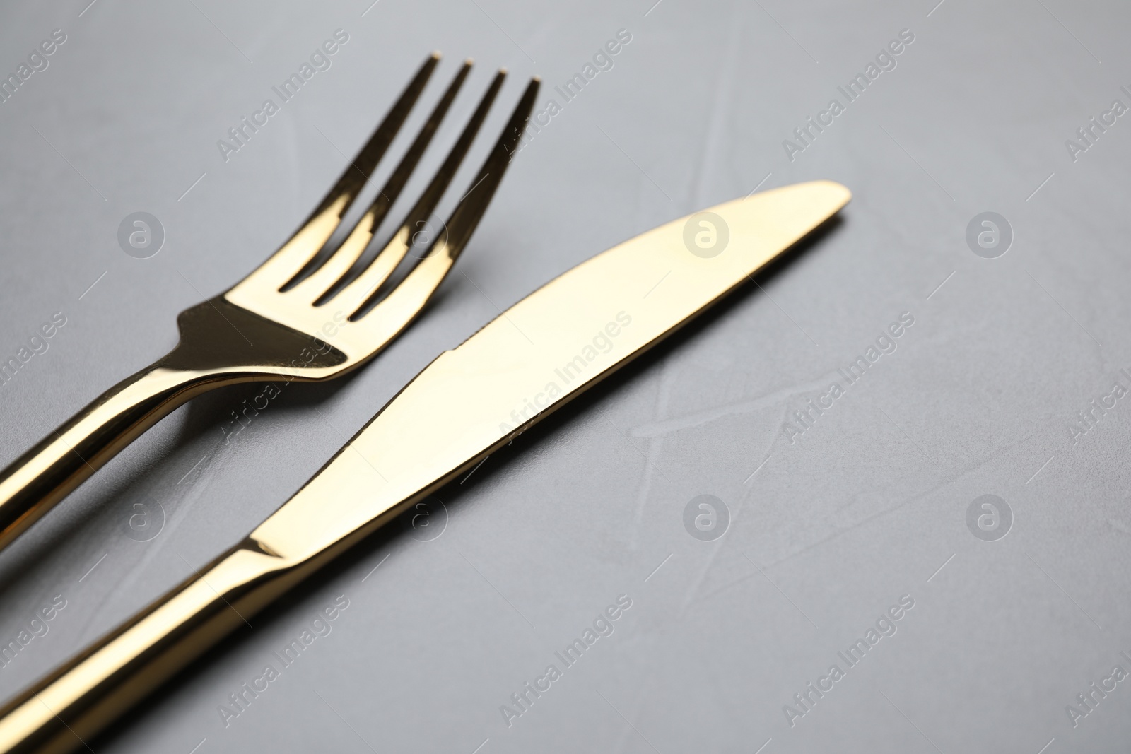 Photo of Golden fork and knife on light grey table, closeup. Space for text