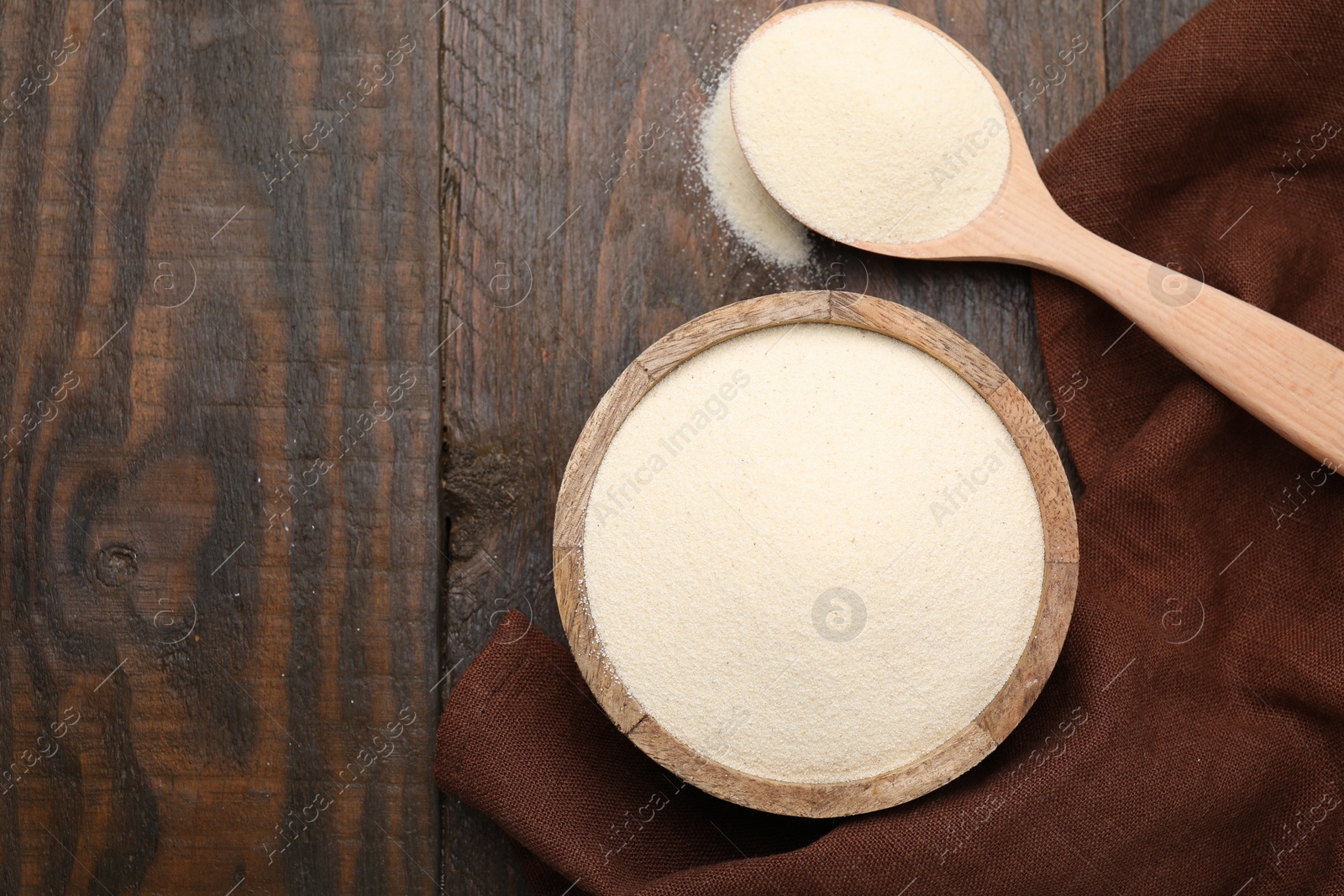 Photo of Uncooked organic semolina in bowl and spoon on wooden table, top view. Space for text