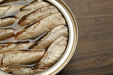 Photo of Sprats in tin can on wooden table, closeup. Space for text