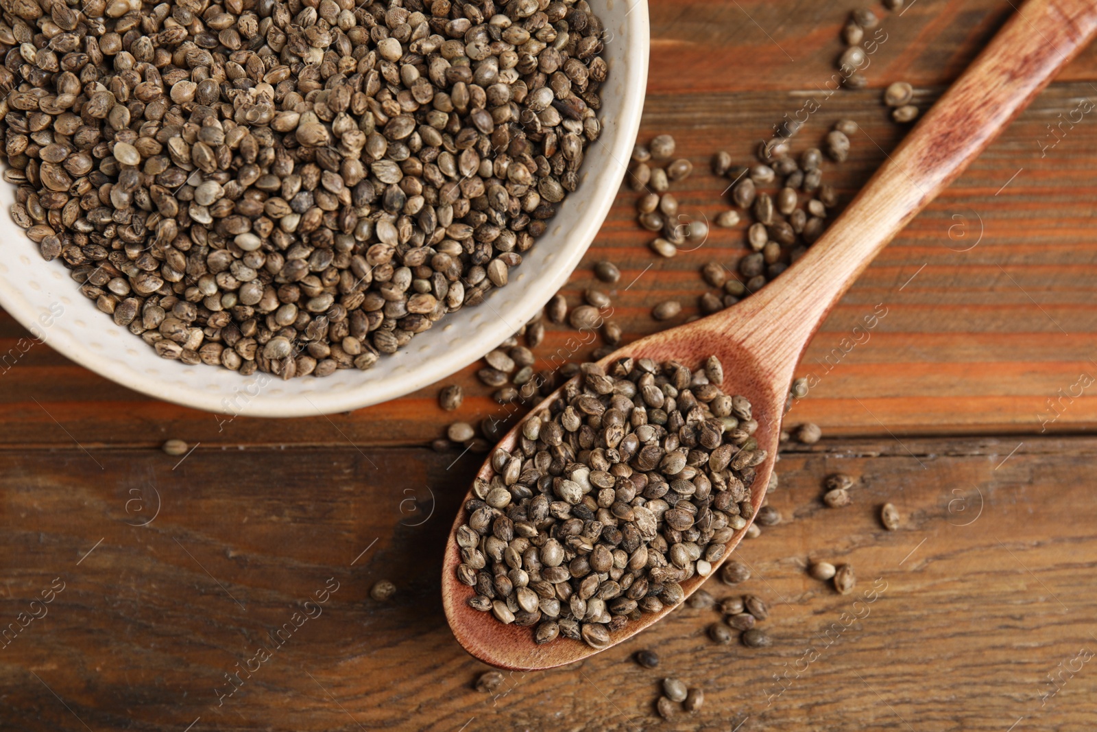 Photo of Bowl and spoon with organic hemp seeds on wooden table, flat lay