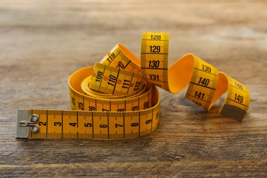 New yellow measuring tape on wooden table, closeup