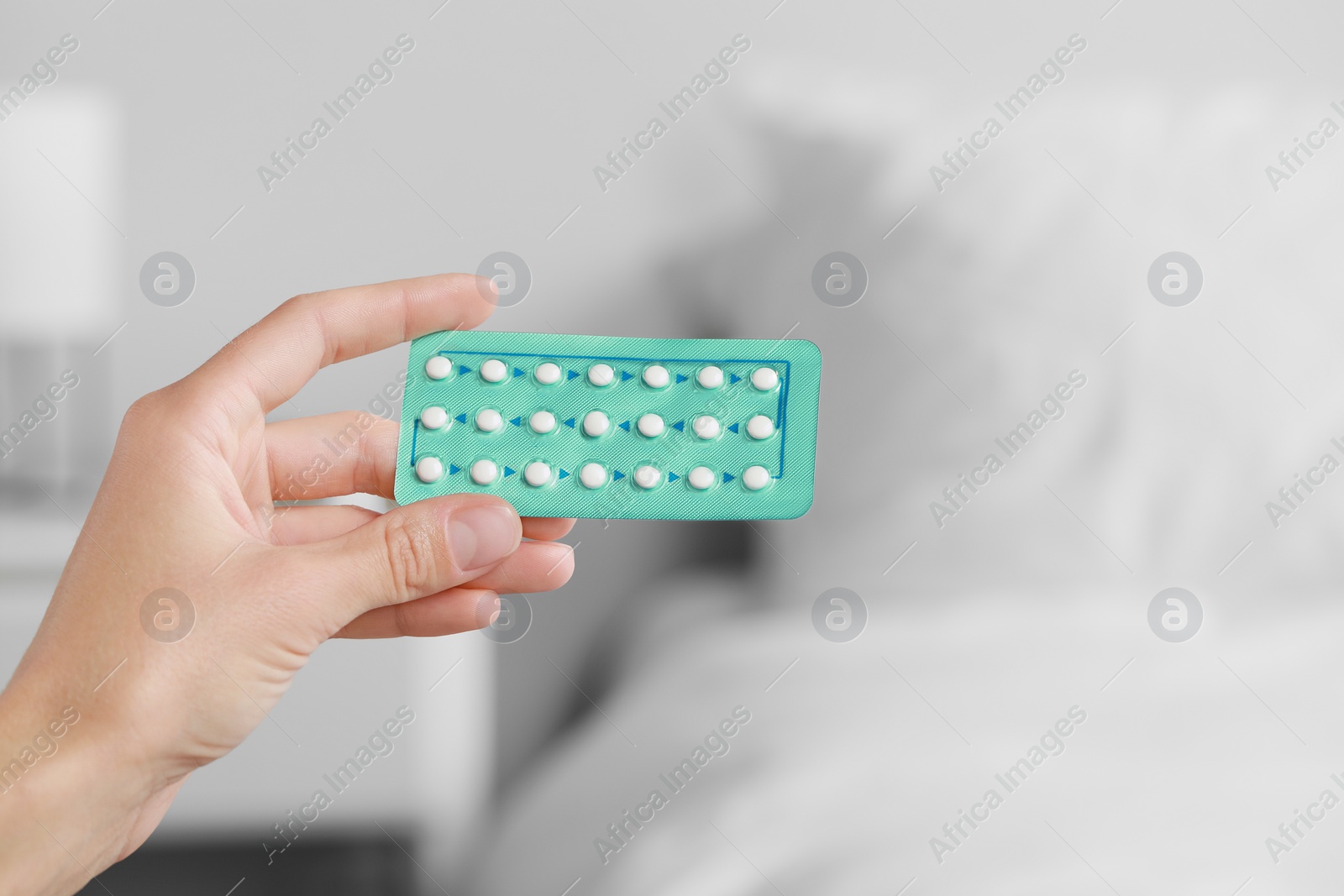 Photo of Woman holding blister of oral contraception pills against blurred background, closeup. Space for text