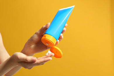 Photo of Woman applying sun protection cream on hand against yellow background, closeup. Space for text