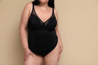 Beautiful overweight woman in black underwear on beige background, closeup with space for text. Plus-size model