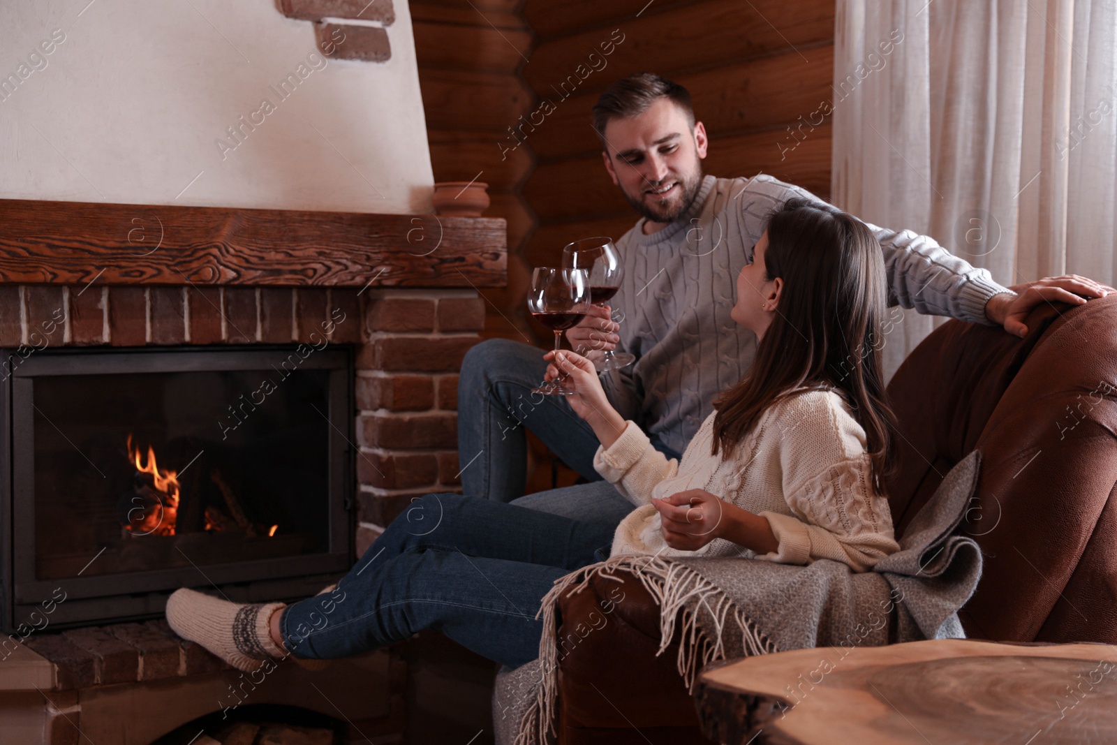 Photo of Lovely couple with glasses of wine resting near fireplace at home. Winter vacation