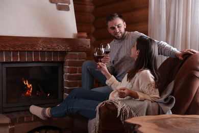 Lovely couple with glasses of wine resting near fireplace at home. Winter vacation