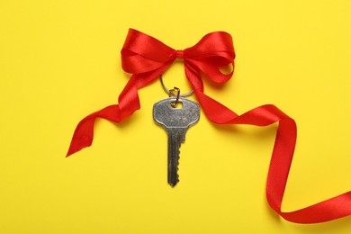 Photo of Key with red bow on yellow background, top view. Housewarming party