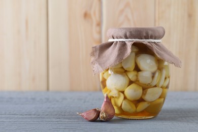 Photo of Garlic with honey in glass jar and unpeeled cloves on grey wooden table. Space for text