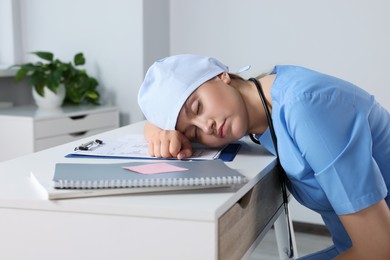 Photo of Tired young doctor sleeping at workplace in office