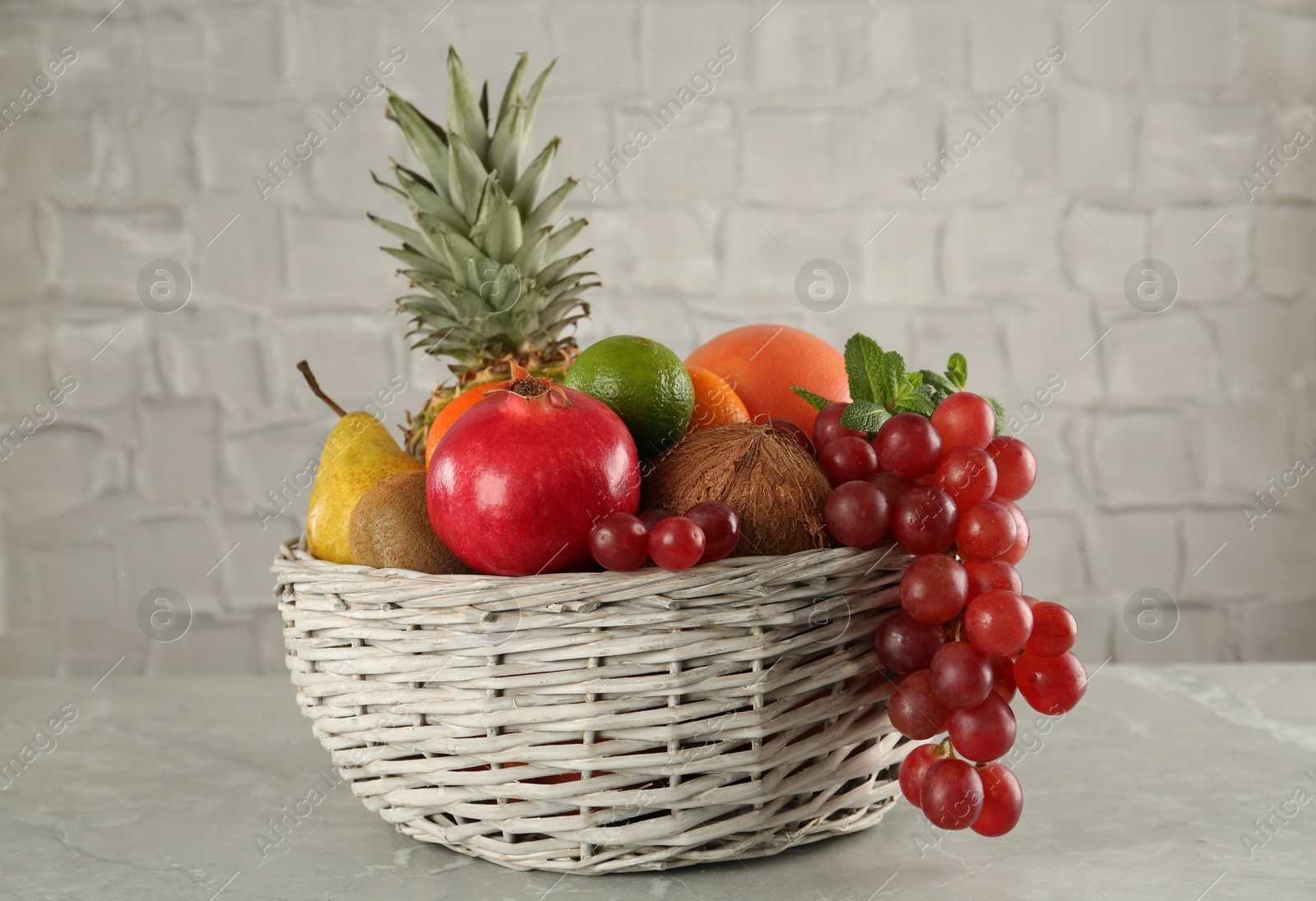 Photo of Wicker basket with different ripe fruits on grey table
