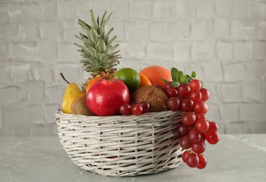 Wicker basket with different ripe fruits on grey table