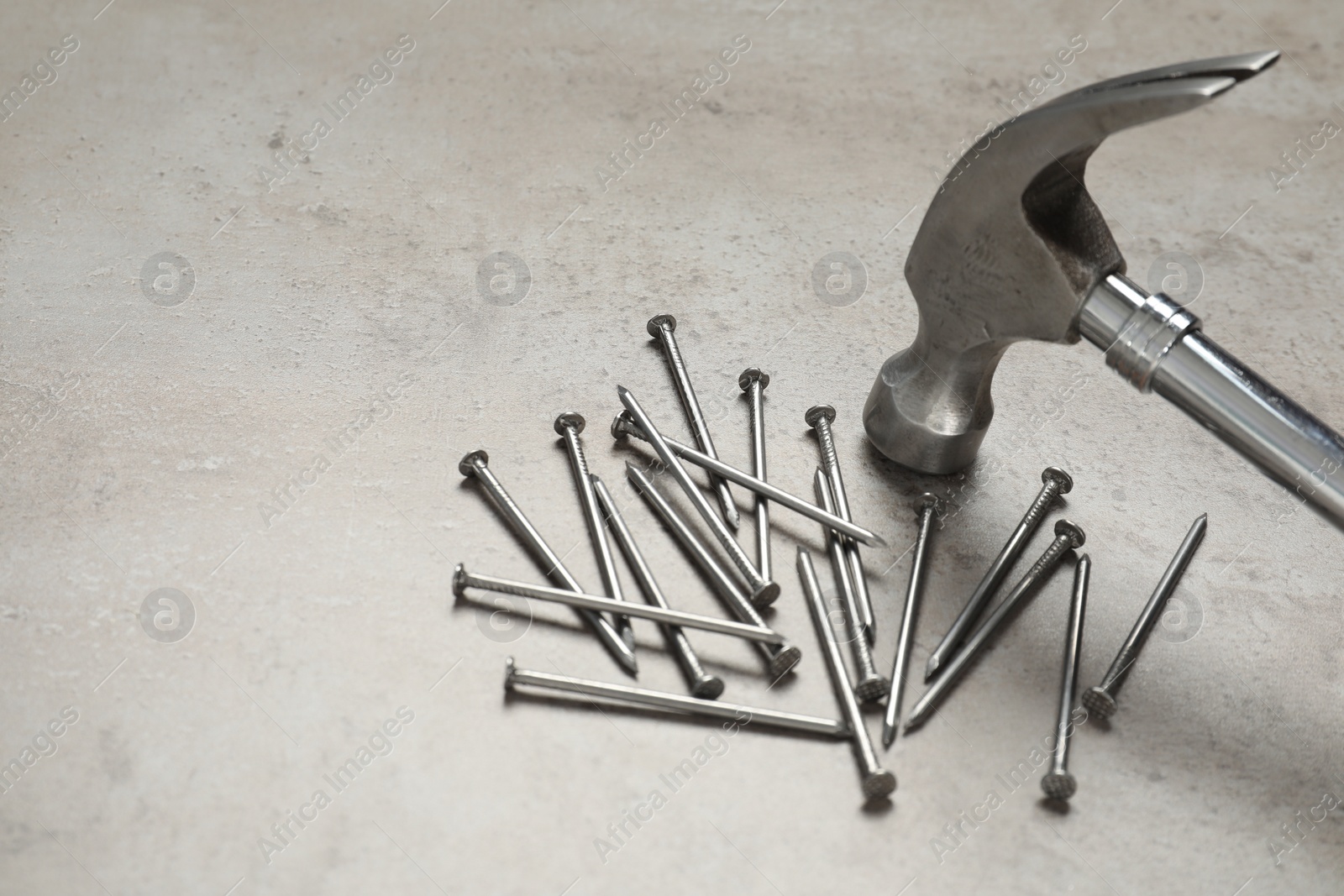 Photo of New hammer and metal nails on grey table. Space for text