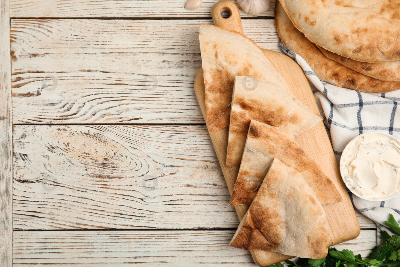 Photo of Cut pita bread, cream cheese and parsley on white wooden table, flat lay. Space for text