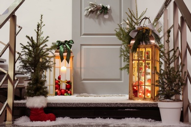 Decorative lanterns and small Christmas trees near house entrance