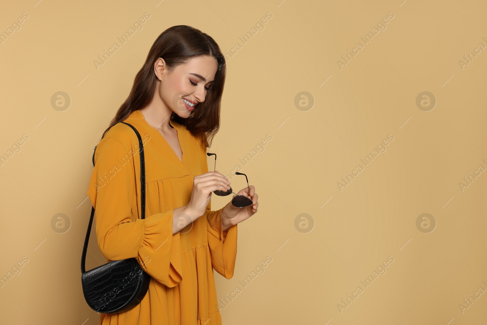 Photo of Beautiful young woman in fashionable outfit with stylish bag on beige background, space for text