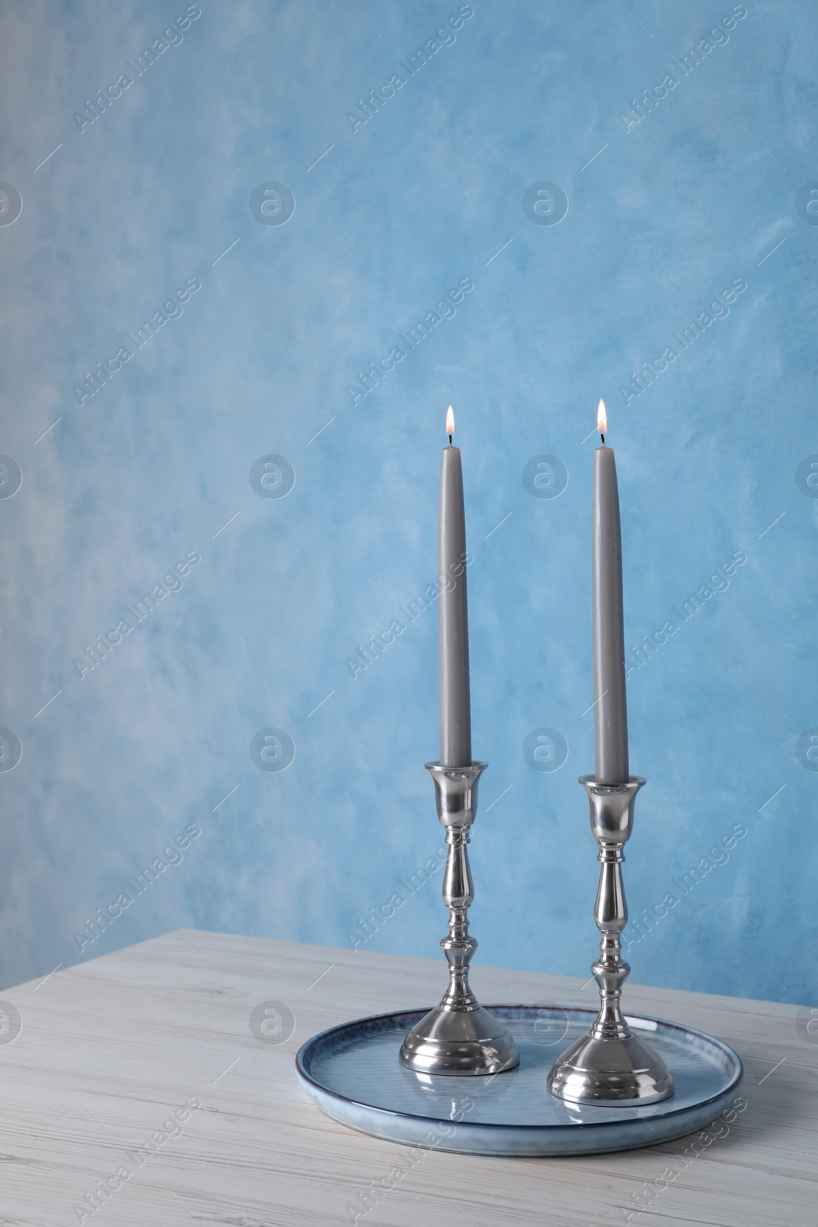 Photo of Holders with burning candles on wooden table near light blue wall, space for text