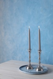 Holders with burning candles on wooden table near light blue wall, space for text