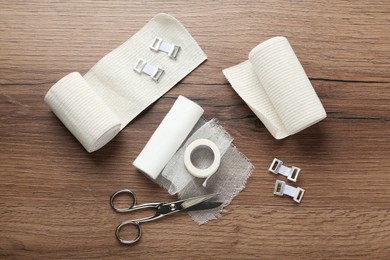 Photo of Medical bandage rolls, sticking plaster and scissors on wooden background, flat lay