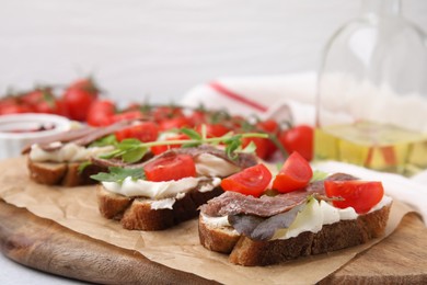 Photo of Delicious bruschettas with anchovies, tomatoes, microgreens and cream cheese on white table, closeup