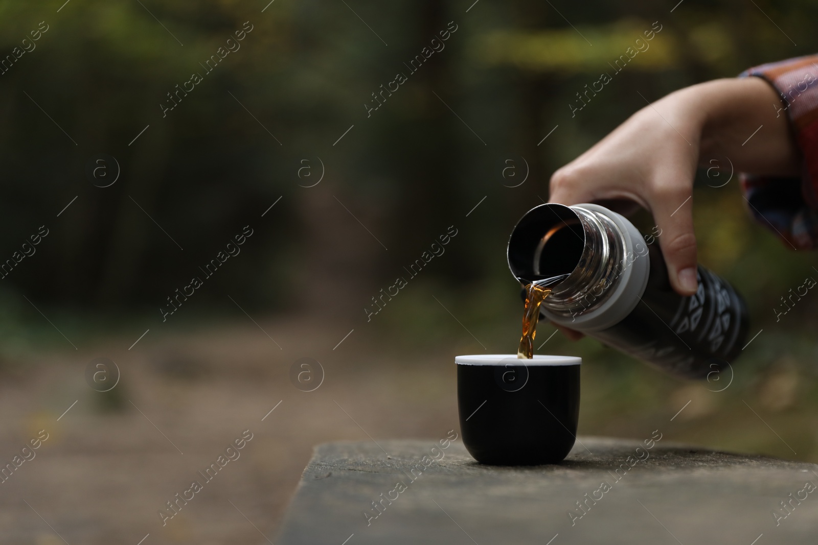 Photo of Woman pouring hot drink from black thermos into cup lid on bench outdoors, closeup. Space for text