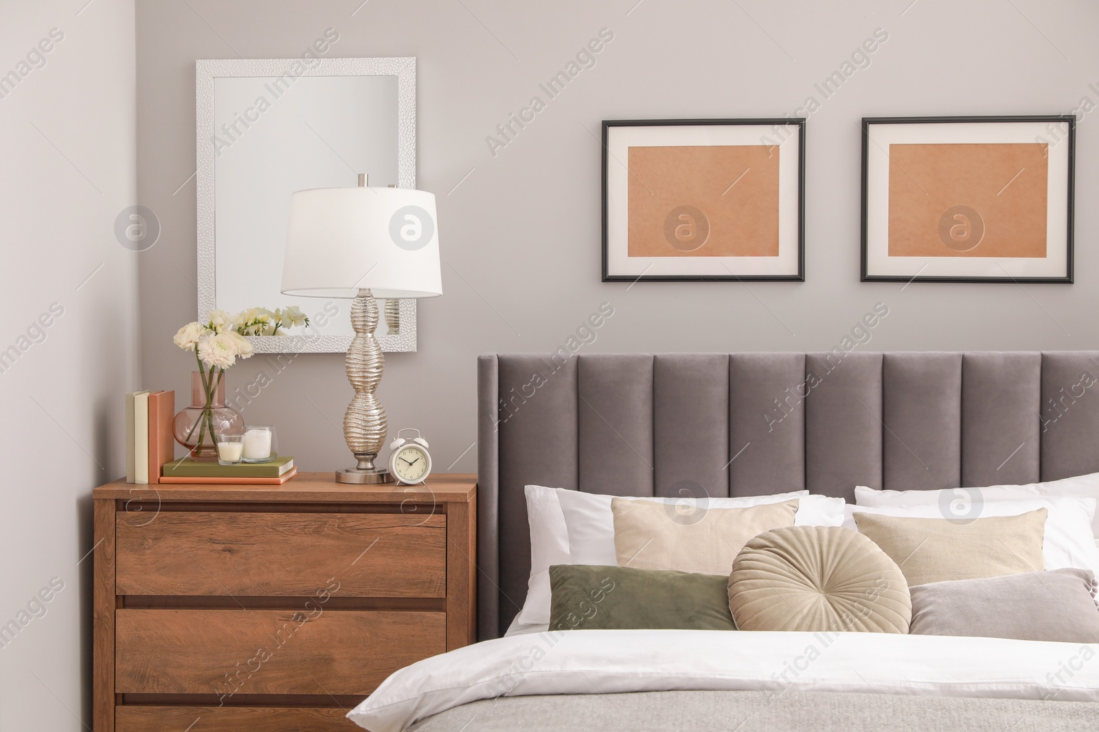 Photo of Comfortable bed with cushions, lamp and different decor on wooden chest of drawers in room. Stylish interior