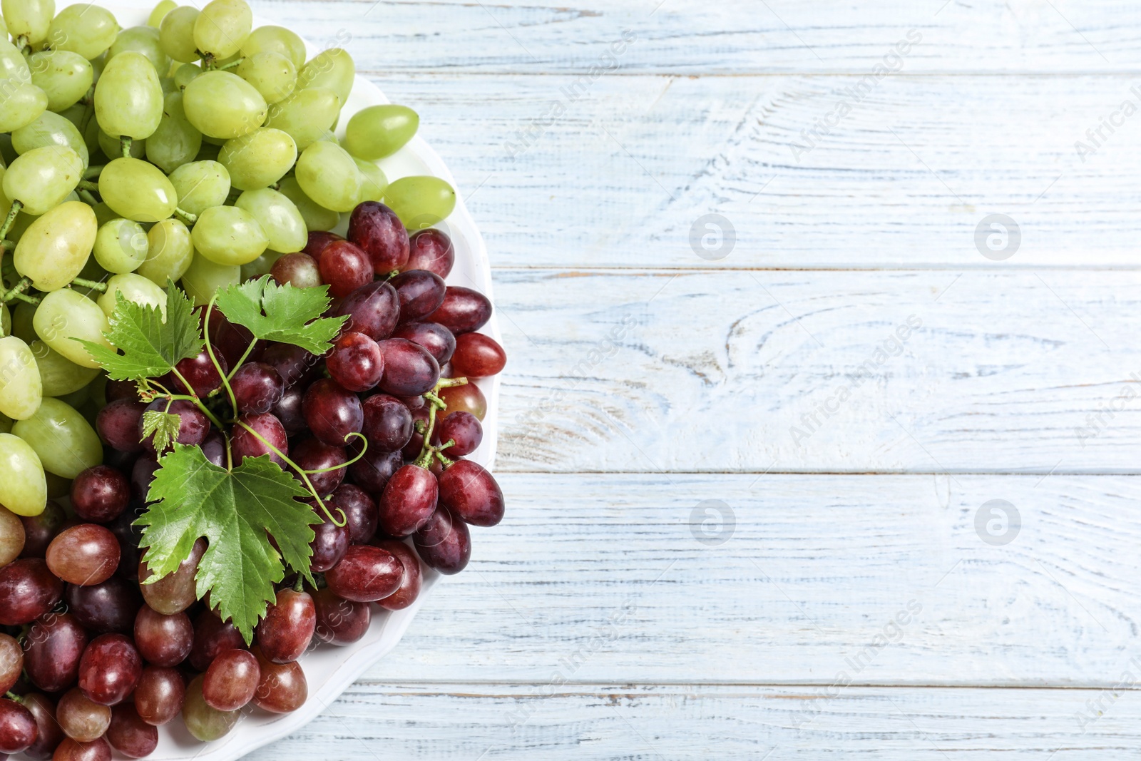Photo of Fresh ripe juicy grapes on white wooden table, top view. Space for text