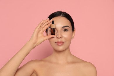 Young woman with bottle of essential oil on pink background