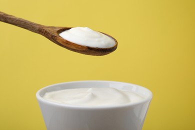 Photo of Eating delicious natural yogurt on yellow background, closeup