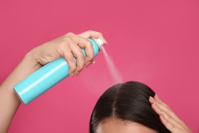 Photo of Young woman applying dry shampoo against pink background, closeup