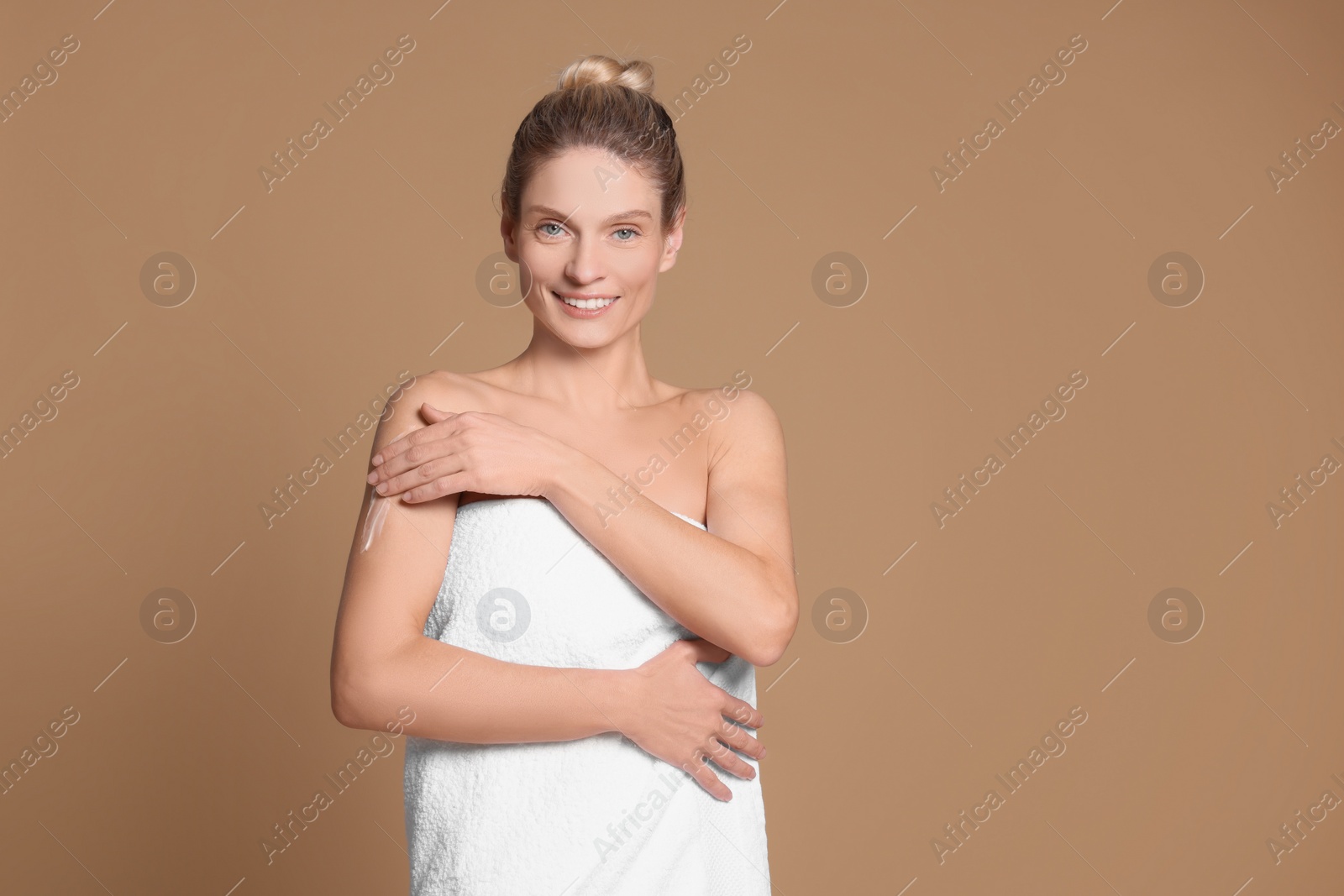 Photo of Woman applying body cream onto her arm against beige background, space for text