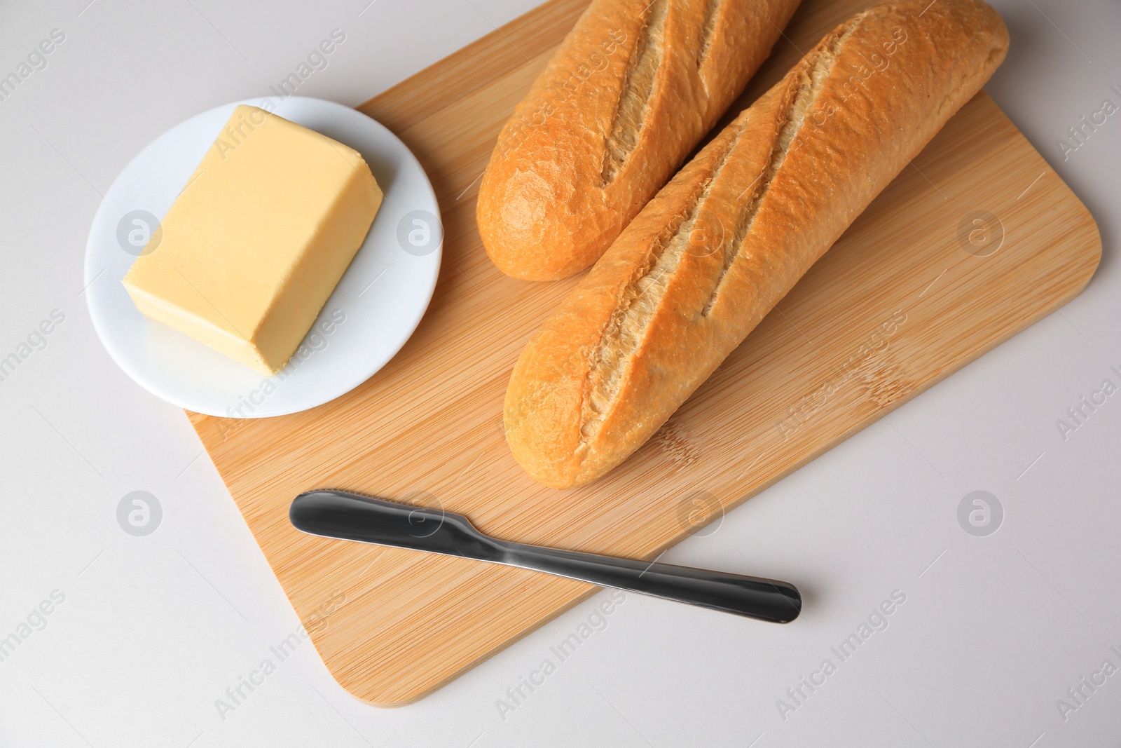 Photo of Tasty baguettes with fresh butter on white table, above view