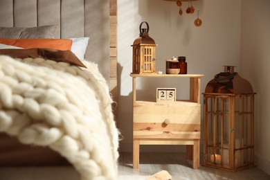 Photo of Vintage lantern and candles on wooden nightstand in bedroom. Interior design