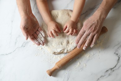 Father and child making dough at white table, top view