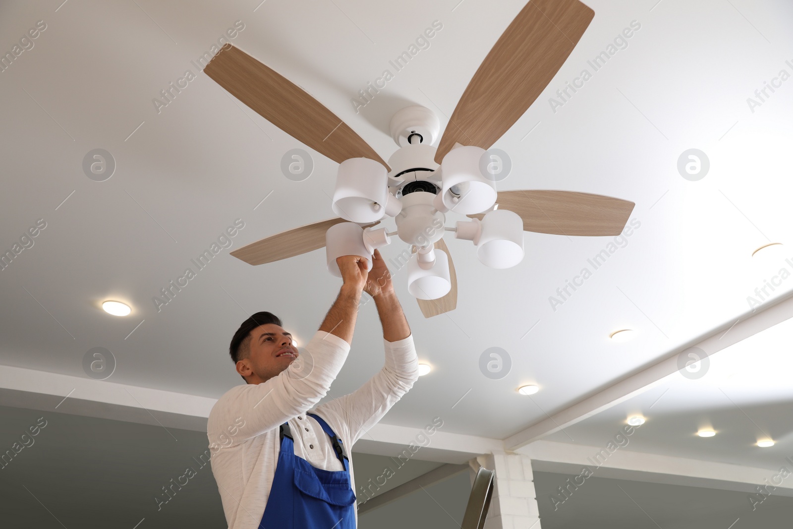 Photo of Electrician changing light bulb in ceiling fan indoors