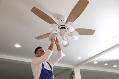 Electrician changing light bulb in ceiling fan indoors