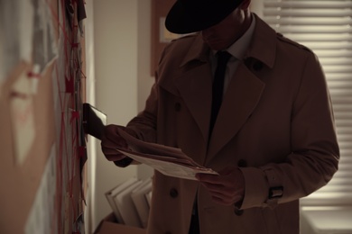 Detective with newspaper near evidence board in office, closeup