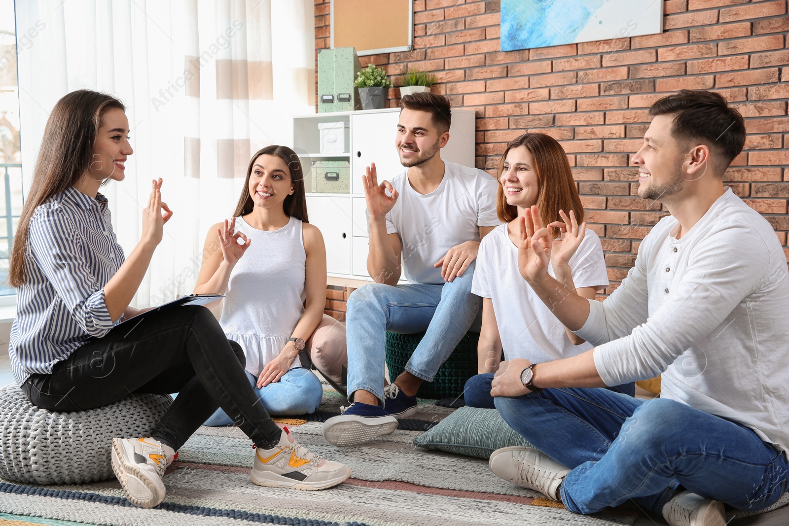 Photo of Group of young people learning sign language with teacher indoors