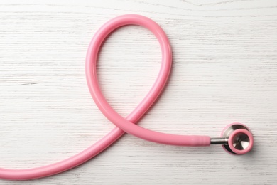 Photo of Pink stethoscope folded like awareness ribbon on wooden background, top view. Breast cancer concept