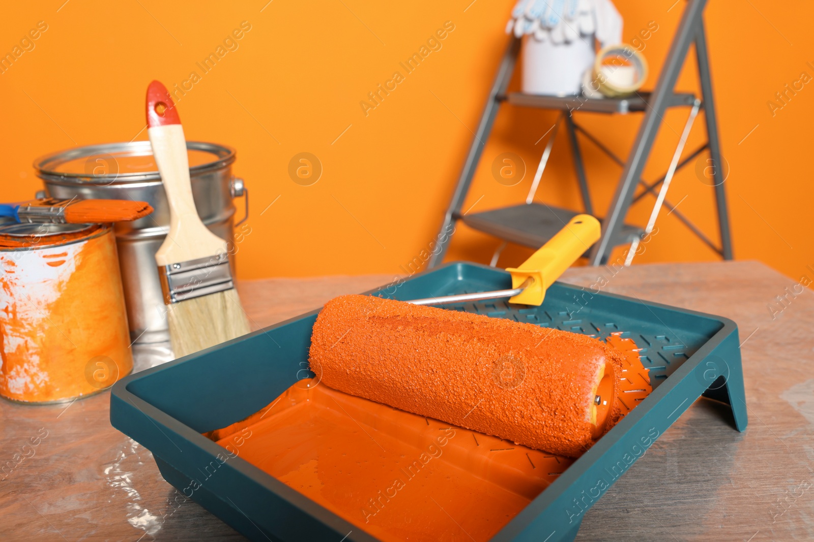 Photo of Tray with orange paint and roller on table, closeup