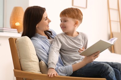 Photo of Mother reading book with her child on armchair at home