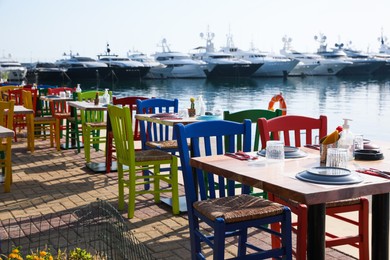 Photo of Beautiful view of outdoor cafe with colorful wooden chairs near pier