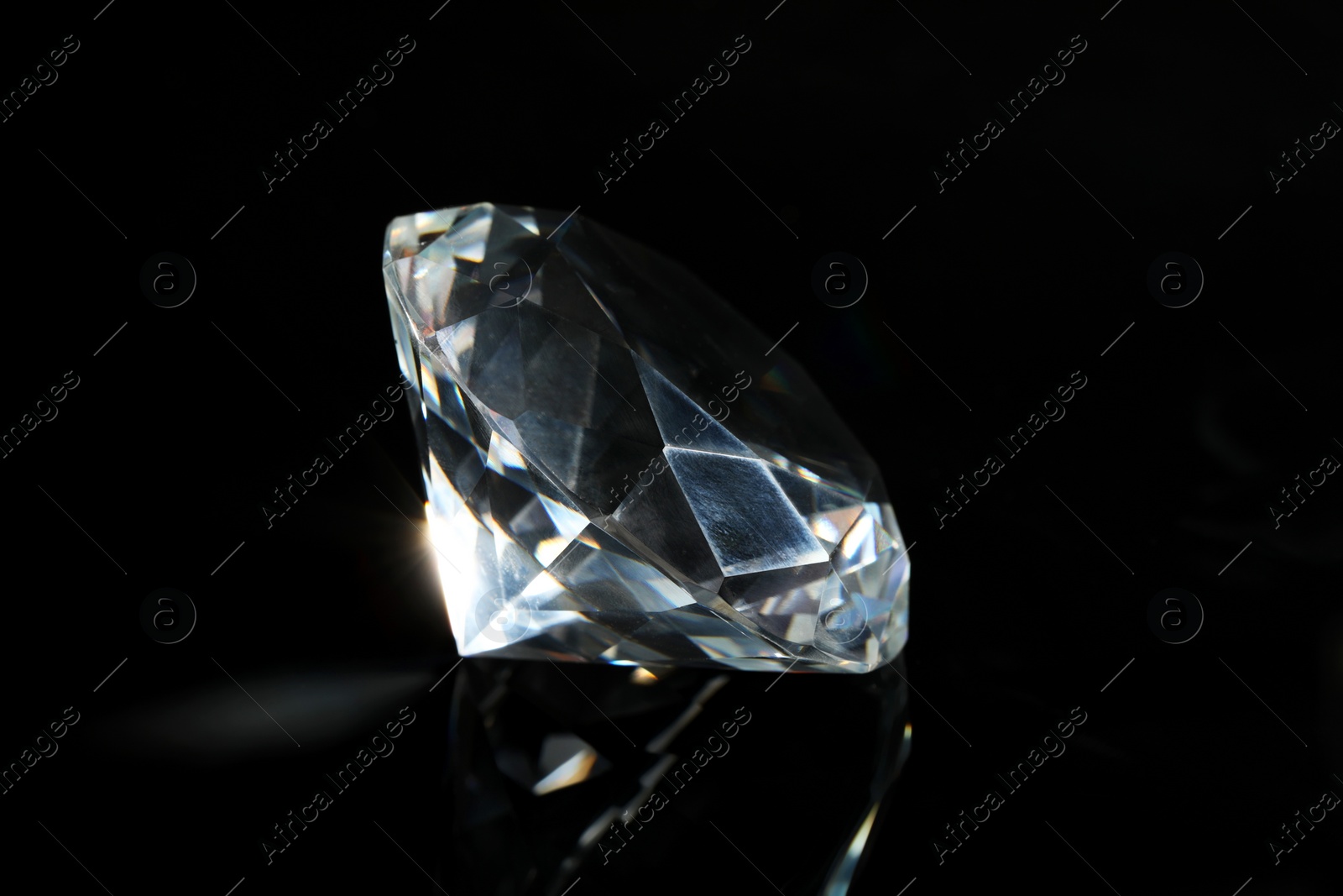 Photo of Beautiful dazzling diamond on black mirror background, closeup