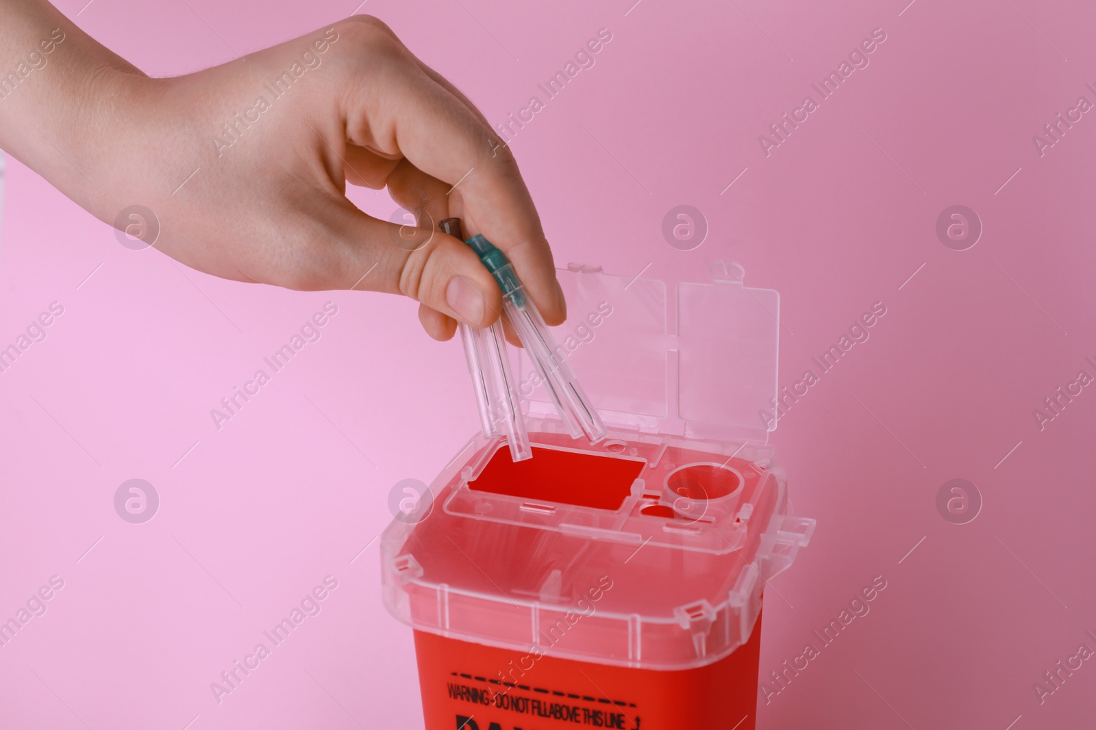 Photo of Woman throwing used syringe needles into sharps container  on pink background, closeup