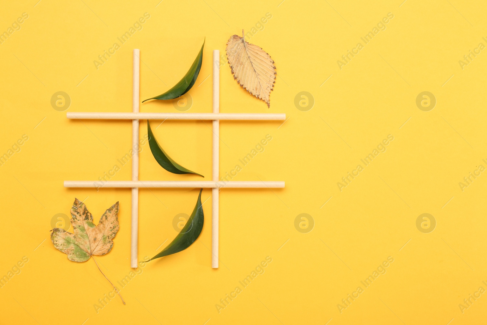 Photo of Tic tac toe game made with fresh and dry leaves on yellow background, top view. Space for text
