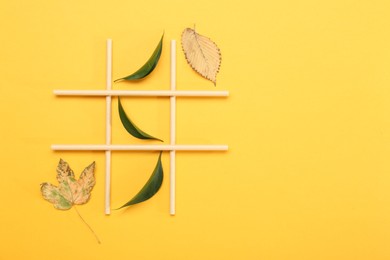 Photo of Tic tac toe game made with fresh and dry leaves on yellow background, top view. Space for text