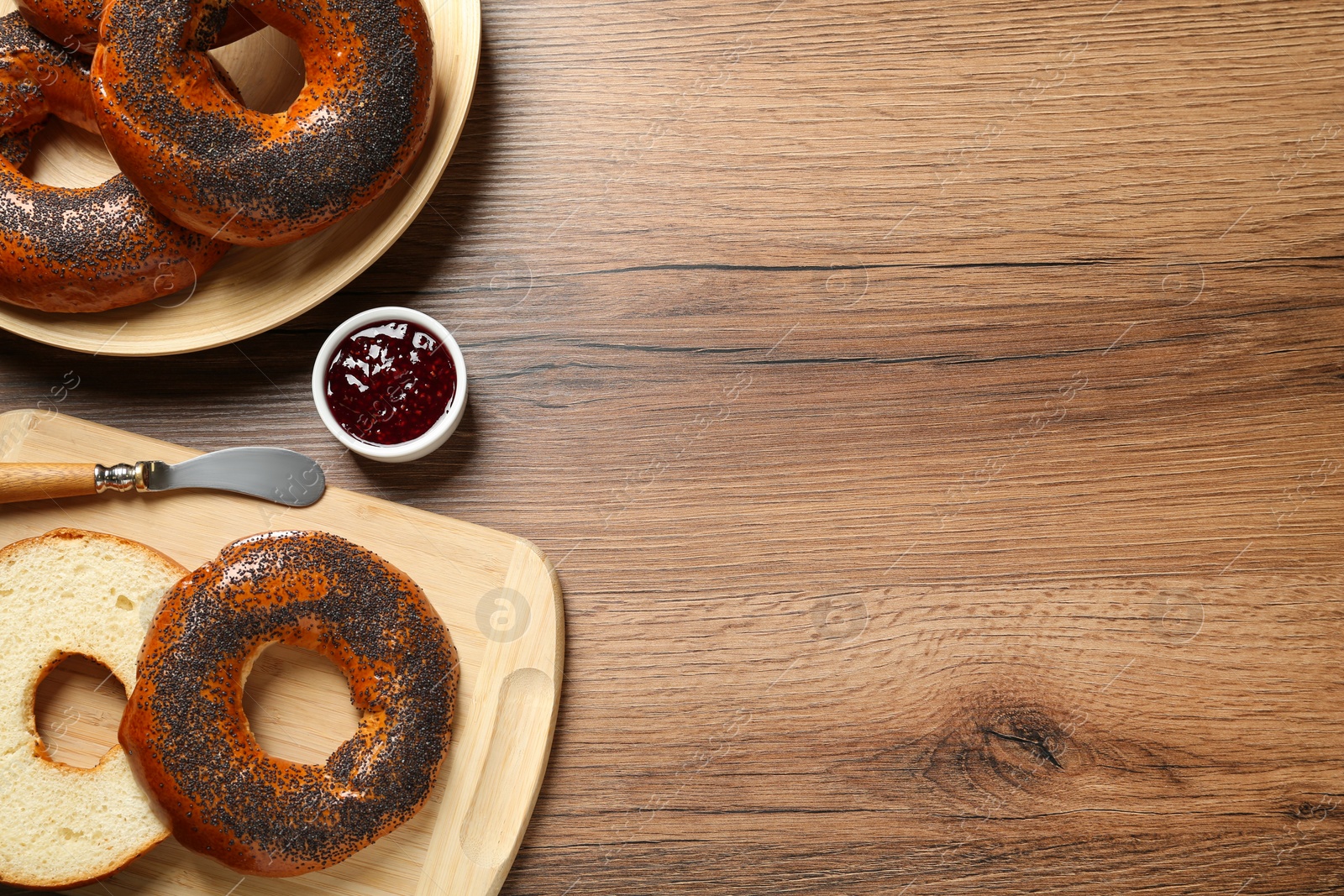 Photo of Delicious fresh bagels with poppy seeds and jam on wooden table, flat lay. Space for text