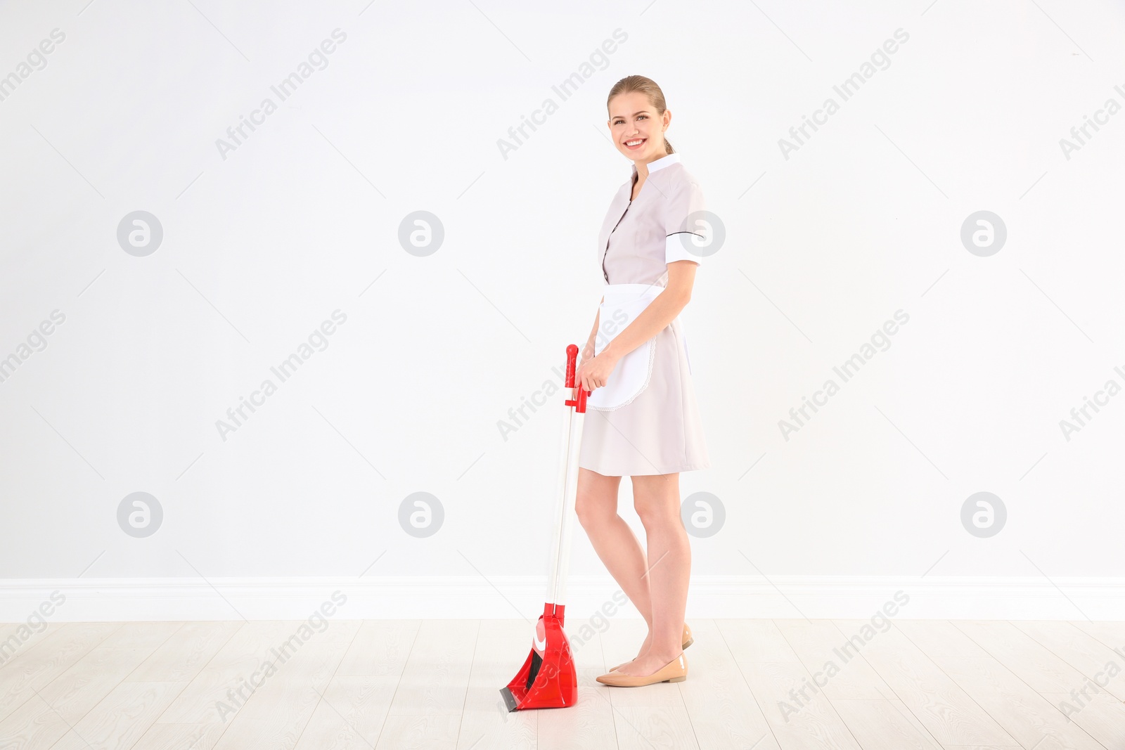 Photo of Young chambermaid with broom and dustpan  indoors