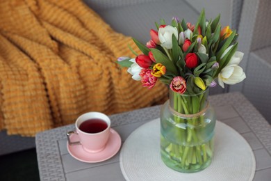 Beautiful bouquet of colorful tulips and cup with drink on rattan garden table
