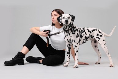 Beautiful young woman with her adorable Dalmatian dog on light grey background. Lovely pet