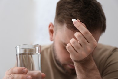 Photo of Man with glass of water and pill suffering from migraine, closeup